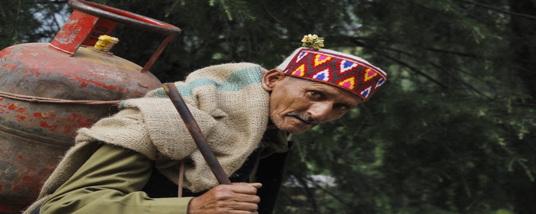A man carrying an LPG gas cylinder on his back in rural India — the human face of India's 2026 energy crisis